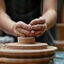 Hands making pottery on a wheel, with digital tablet in background, symbolizing integration